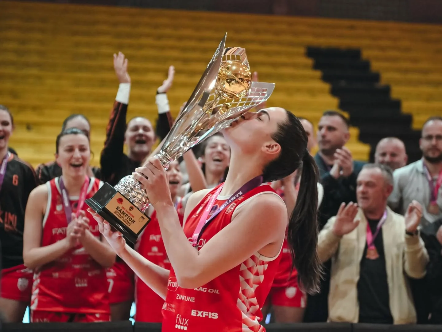 Një lojtare e KBF Bashkimit puth trofeun e kampioneve, me shoqet që festojnë pas saj